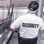 Security Officer wearing a white shirt with black pants, going down an escalator